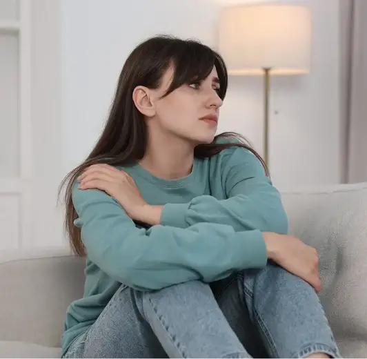 A concerned young woman sitting on a couch, illustrating the symptoms of stress and worry