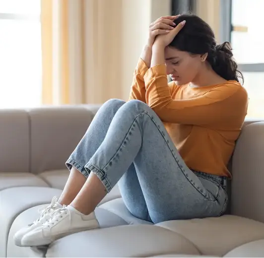 A woman sitting on a sofa with her head in her hands, depicting signs of emotional distress
