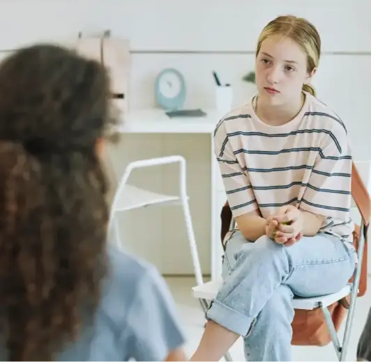 A young girl in a striped shirt sitting in a counseling session, illustrating a wellness assessment